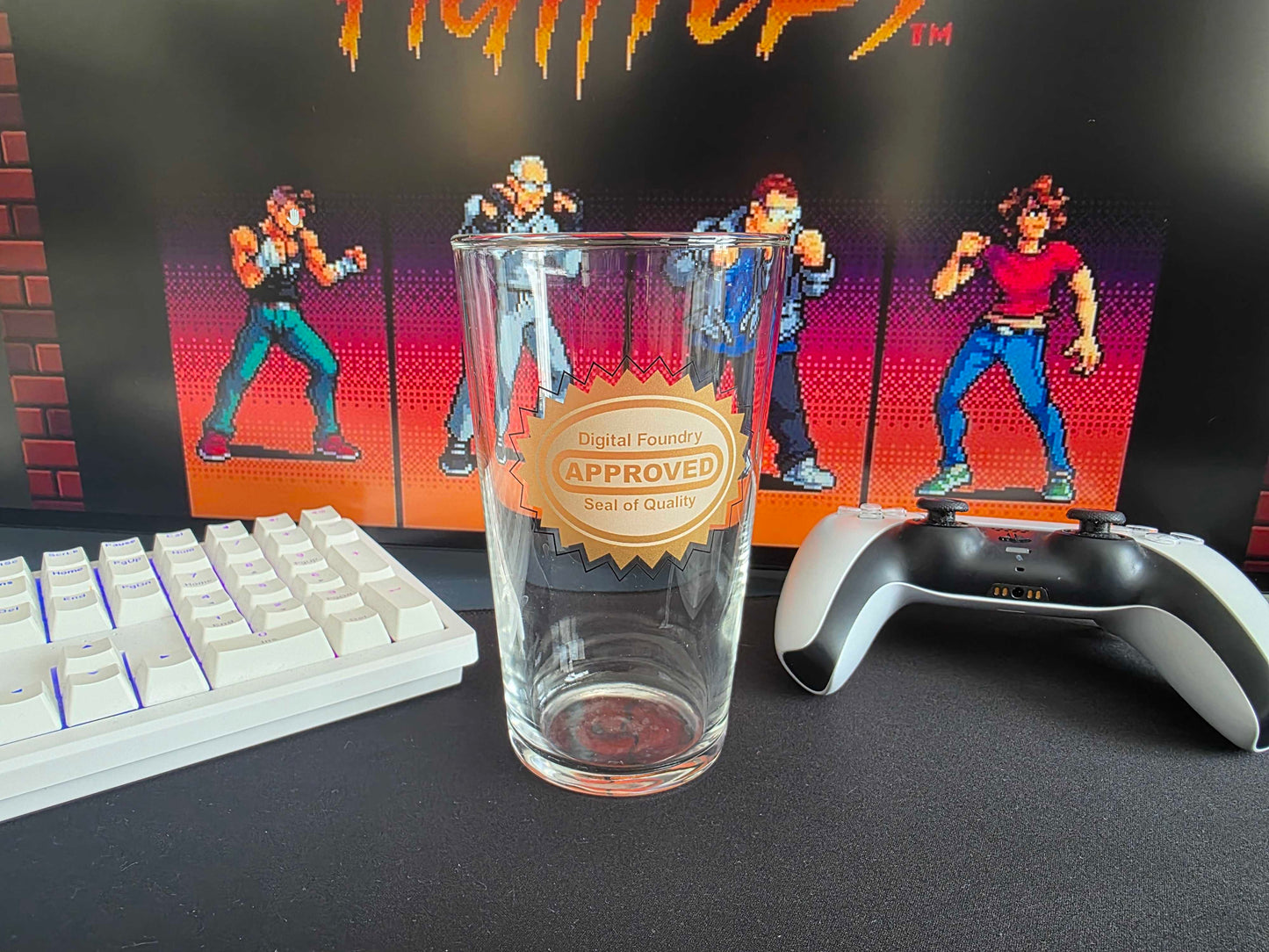 A clear glass drinking tumbler with a gold seal reading 'DF Approved Seal of Quality' in the center, set on a dark desk alongside a white mechanical keyboard and a black-and-white game controller, with a Fight Nights arcade-style backdrop.